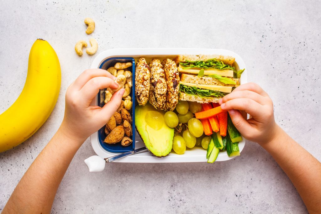 A child eating lunch filled with a sandwich, vegetables and fruit snacks